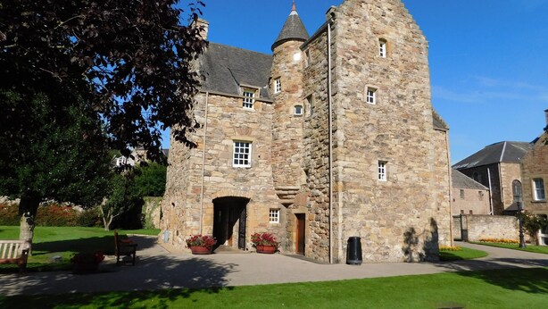 A stone building with a central tower, a large arched entrance, and a paved courtyard. - Cottage in Jedburgh With Stunning Views (Jedburgh)