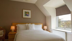 A bedroom with a bed, two bedside lamps, a framed picture on the wall, a window with a view, and a sloped ceiling. - Cottage in Jedburgh With Stunning Views (Jedburgh)
