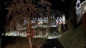 Un edificio grande e iluminado con varios tejados a dos aguas, rodeado de árboles y una valla.