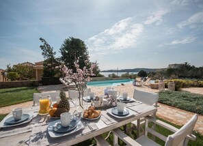 An outdoor dining area with a pool view, a table set with breakfast, and a clear sky.