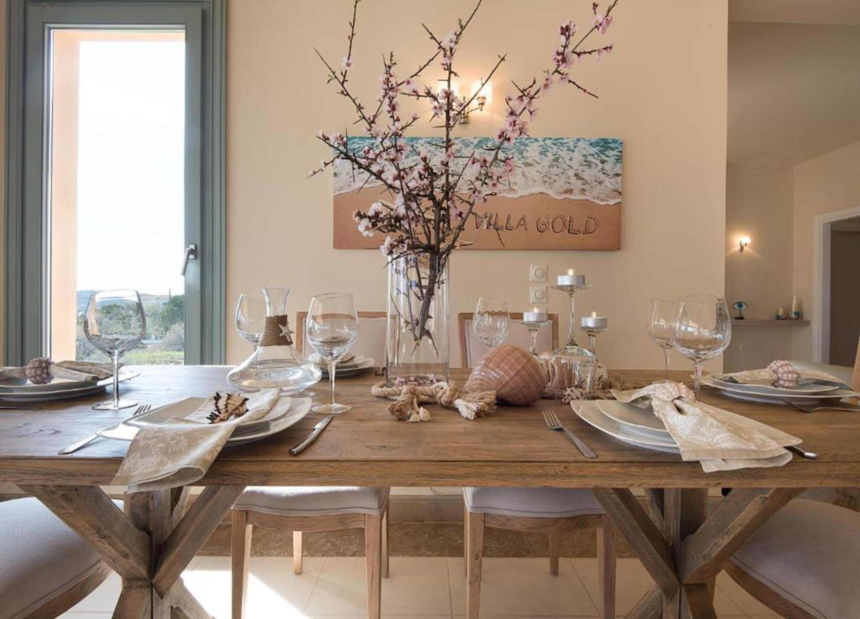 A dining table set for six with a vase of branches and a painting in the background.