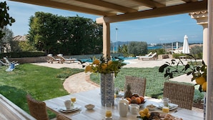 A covered outdoor dining area with a view of a swimming pool and greenery.
