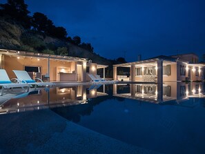 Ein modernes Haus mit Swimmingpool, Liegestühlen und Barbereich.