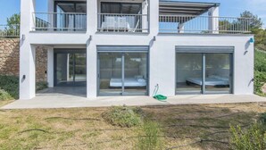 A modern two-story house with large sliding glass doors, a balcony, and a stone wall foundation. - Holiday Home in Porto Heli for 6 Guests (Ermionida)