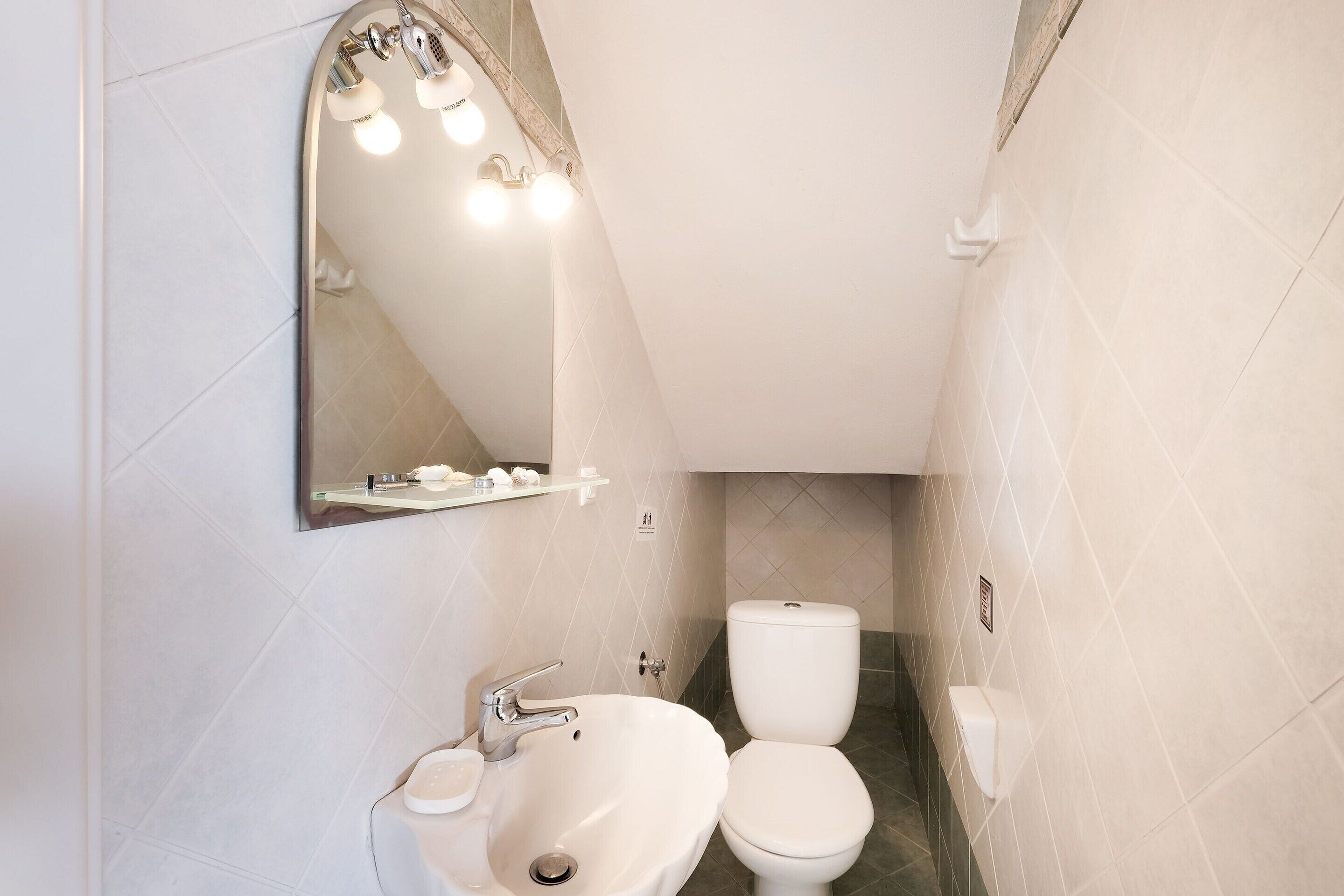 A bathroom with a white sink, a toilet, and a mirror with lights.