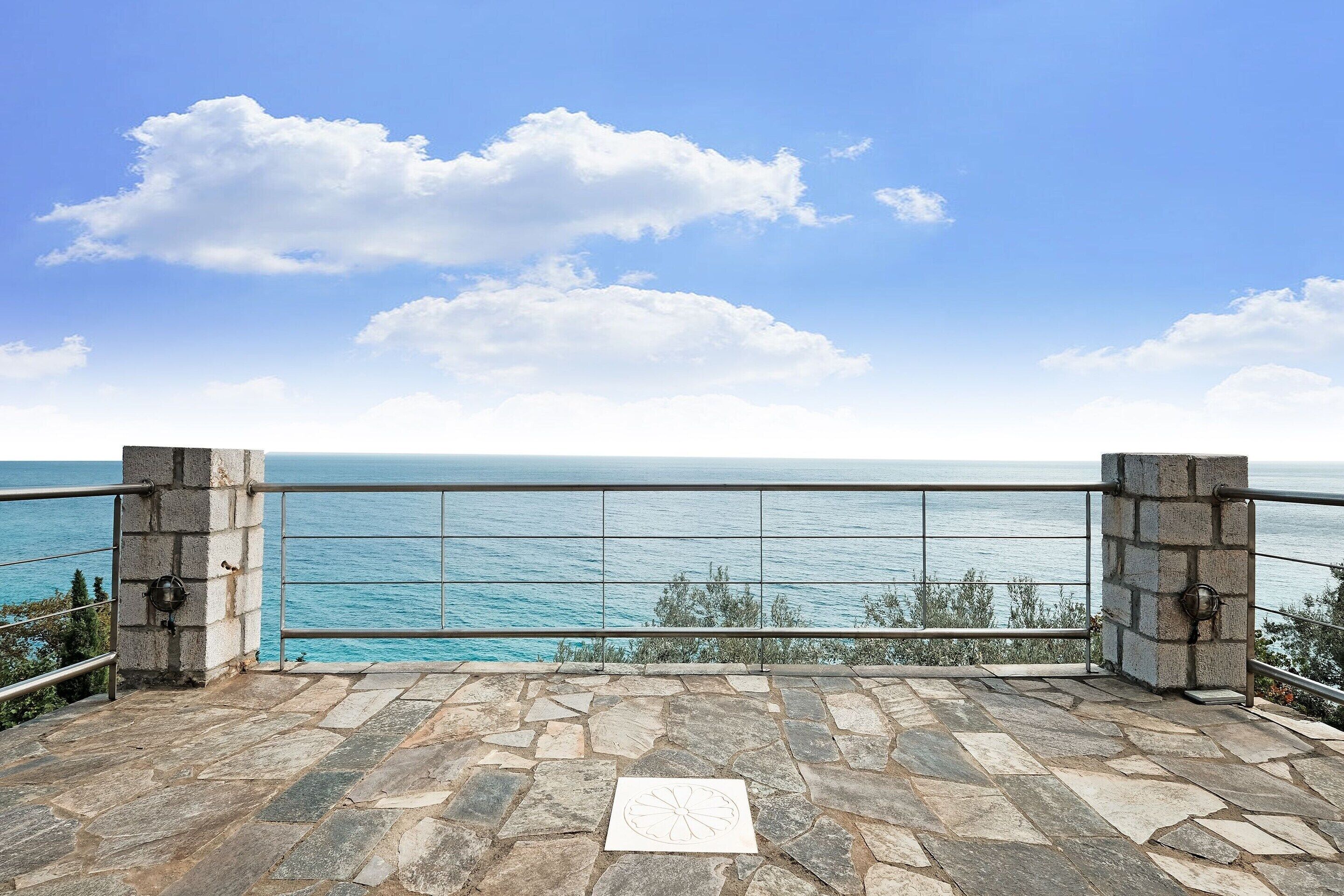 A stone balcony with a metal railing overlooking a body of water.