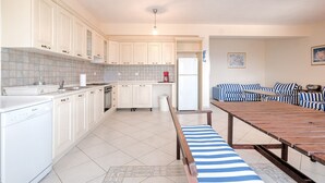 A modern kitchen with white cabinets, a dishwasher, and a dining area with a striped bench. - Villa in Pera Melana Near Kissakas Beach (South Kynouria)