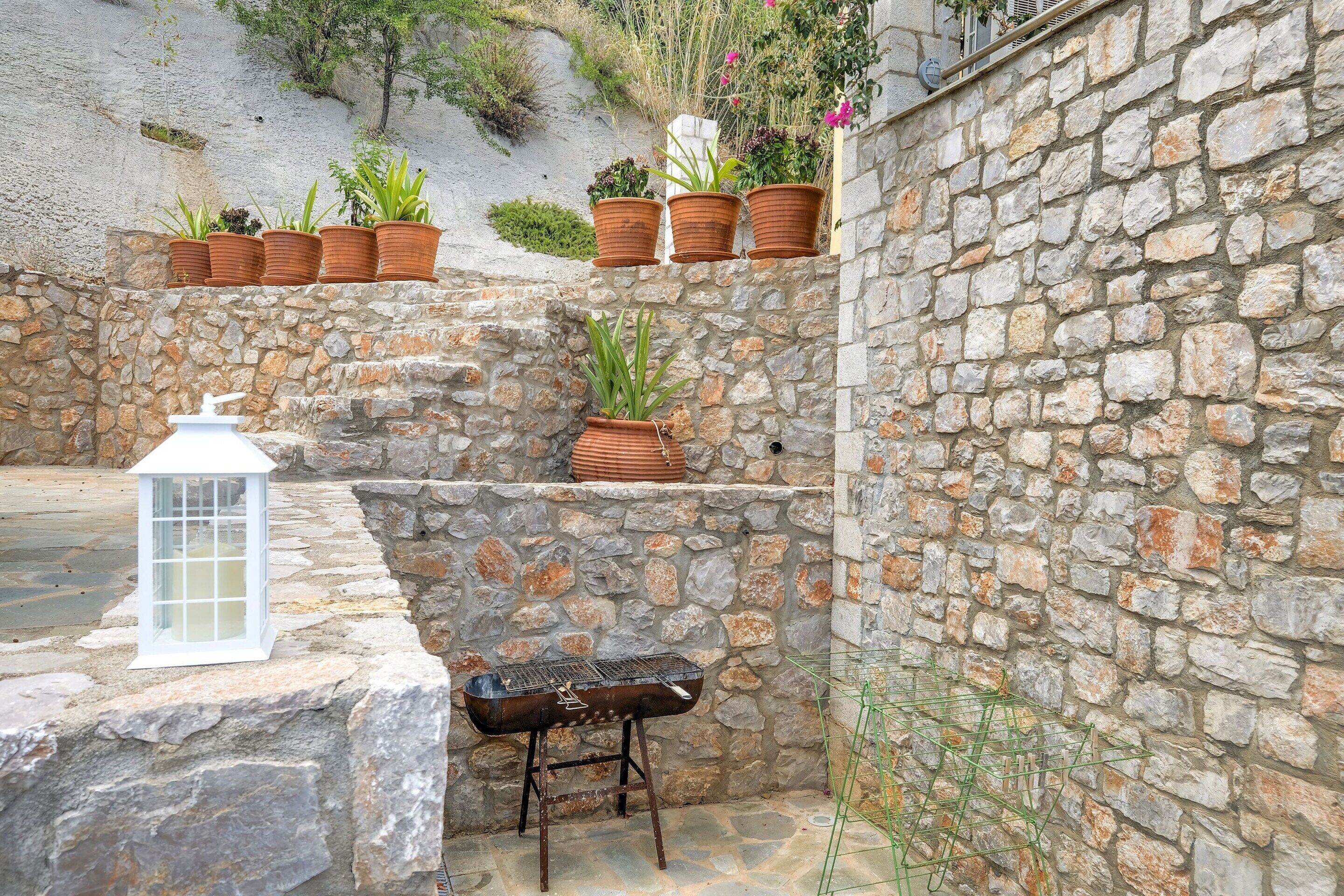 A stone wall with potted plants, a lantern, and a grill.