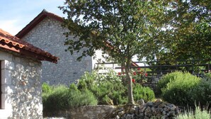 A stone building with a tiled roof, surrounded by a garden with various plants and flowers. - Chalet in Leonidio Near Mount Parnon (South Kynouria)