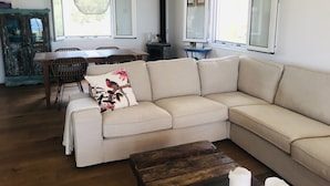 A living room with a beige sectional sofa, a wooden coffee table, and a dining area with a wooden table and wicker chairs. - Luxurious Villa in Peloponnese (Pylos-Nestoras)