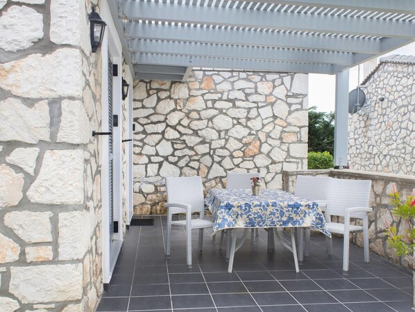 An outdoor patio with stone walls, a covered seating area, and a table with a patterned tablecloth. - Lovely Villa in Complex of 2 Separate Villas near Laganas Sandy Beach (Zakynthos)