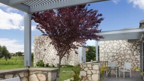 An outdoor patio with a stone wall, a covered seating area, and a small tree with red leaves.