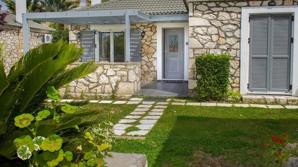 A stone house with a tiled roof, a covered porch, and a well-maintained garden.