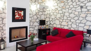 A cozy living room with a stone wall, a fireplace, a red sofa, and a TV.