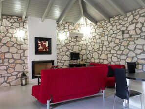 A living room with a stone wall, a fireplace, a red sofa, and a TV.