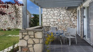Ein überdachter Patio-Bereich mit Steinmauern, einem Tisch mit Stühlen und einer Pergola.