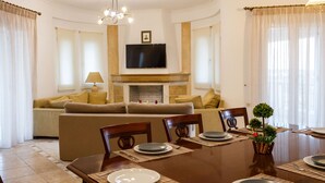 Zona pranzo con tavolo in legno apparecchiata per quattro persone, divano e televisione sopra un camino.