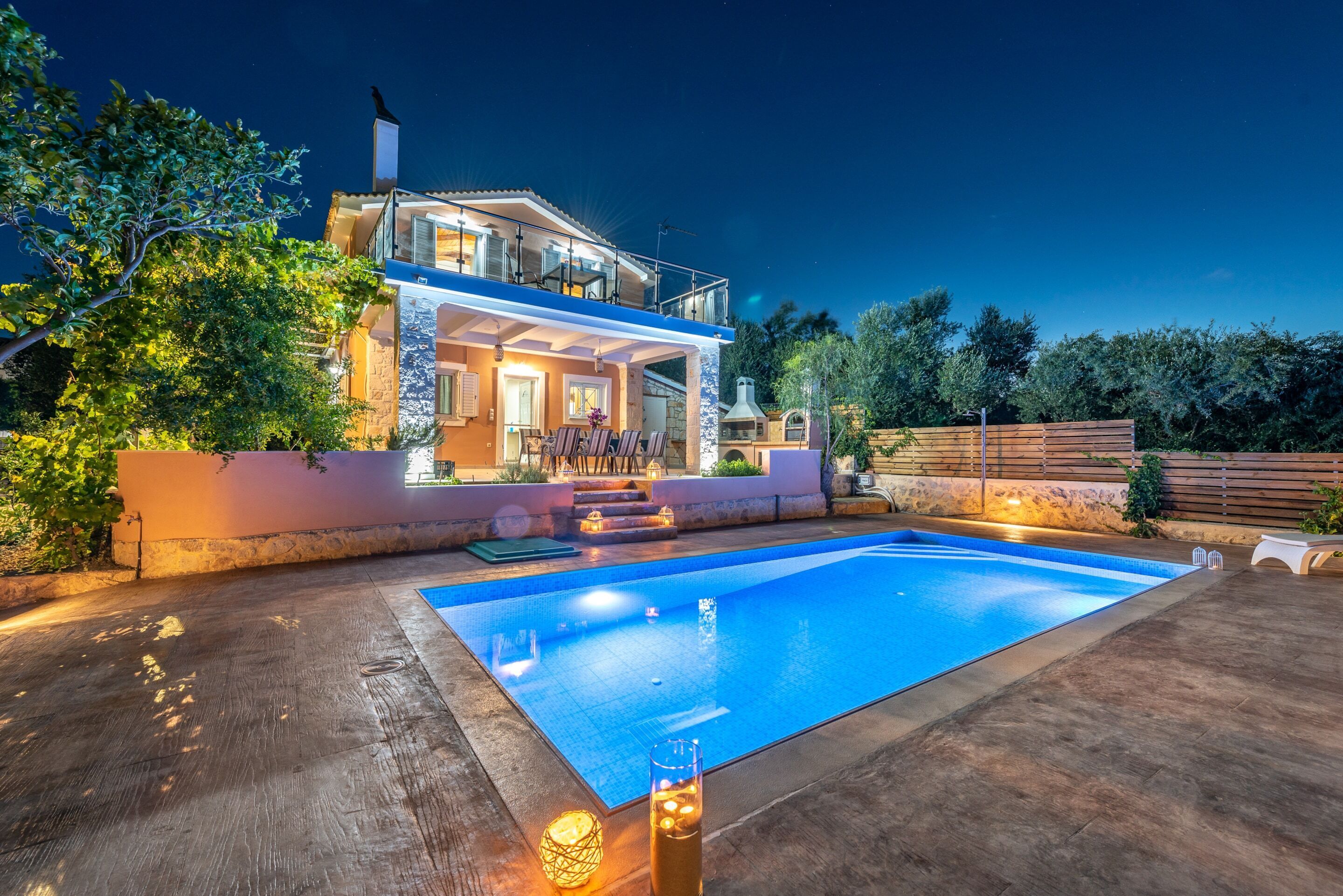 A two-story house with a swimming pool, outdoor seating, and a wooden fence.