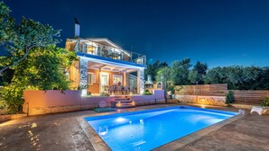 Una casa a due piani con piscina, area salotto esterna e recinzione in legno.