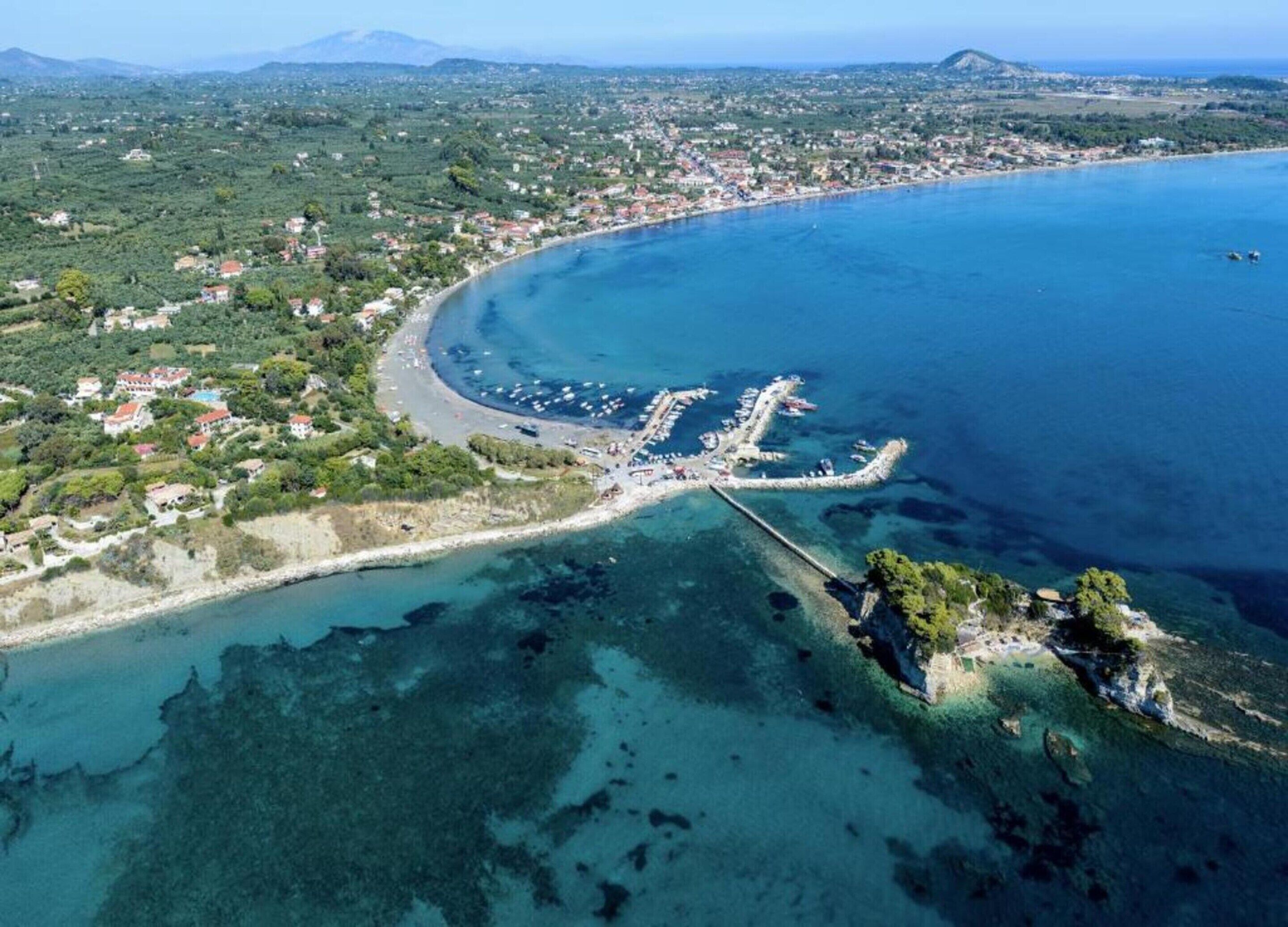 An aerial view of a coastal town with a marina, clear blue waters, and surrounding greenery.