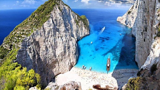 Paesaggio costiero con spiaggia stretta, scogliere rocciose e acque cristalline blu.