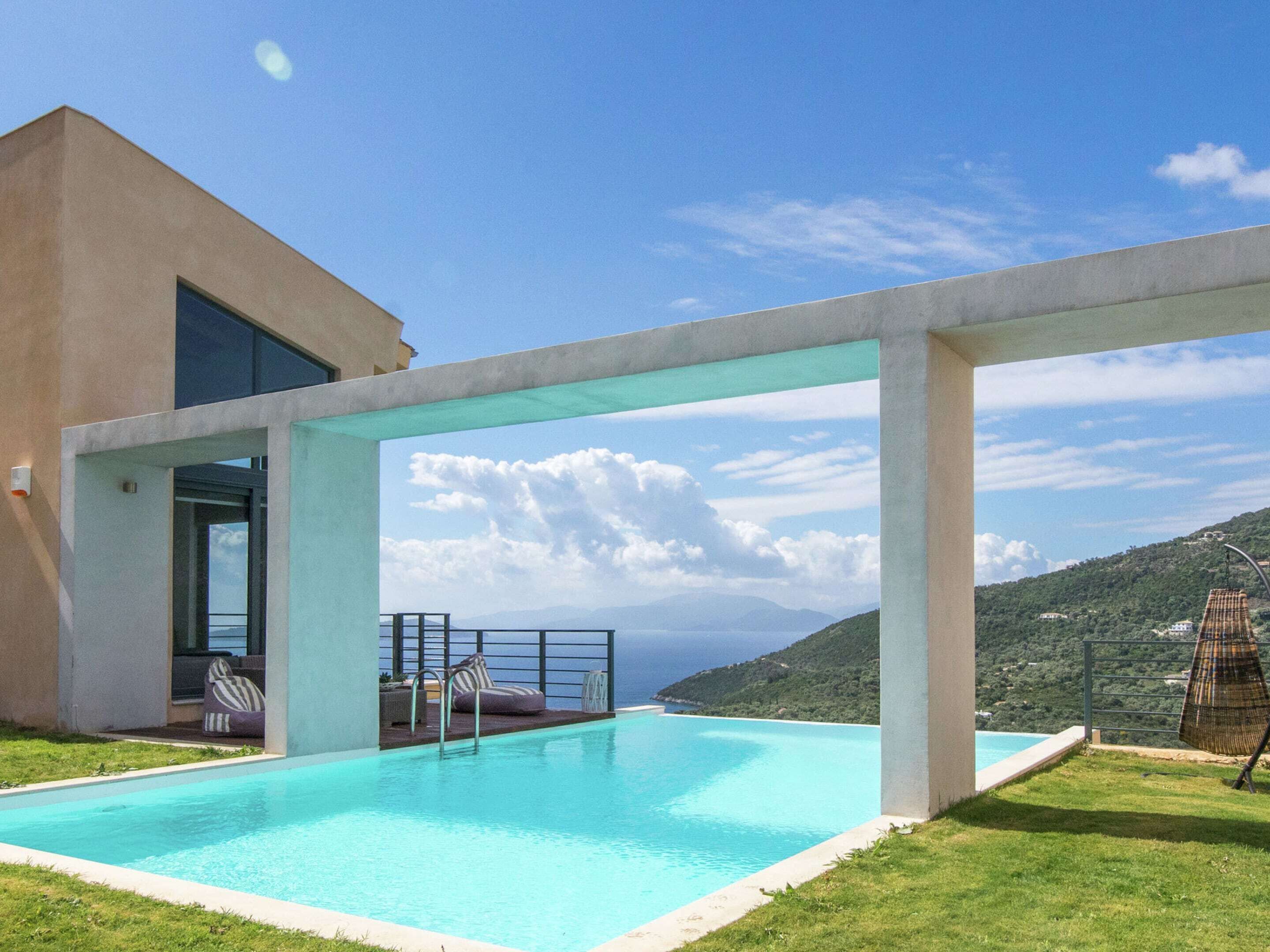 Une piscine extérieure moderne offrant une vue dégagée sur la mer et les collines en arrière-plan.
