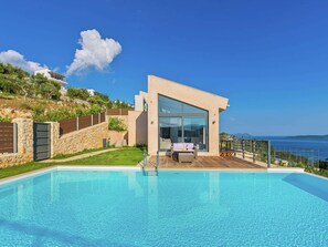 Una casa moderna con piscina, un patio con mobiliario exterior y vista al mar.