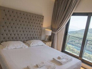 Habitación de hotel con una cama grande, una mesita de noche con lámpara y vistas a un paisaje por la ventana.