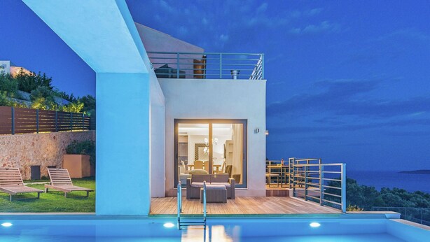 Un'area piscina moderna con una zona relax in vetro, posti a sedere all'aperto e vista sul mare.