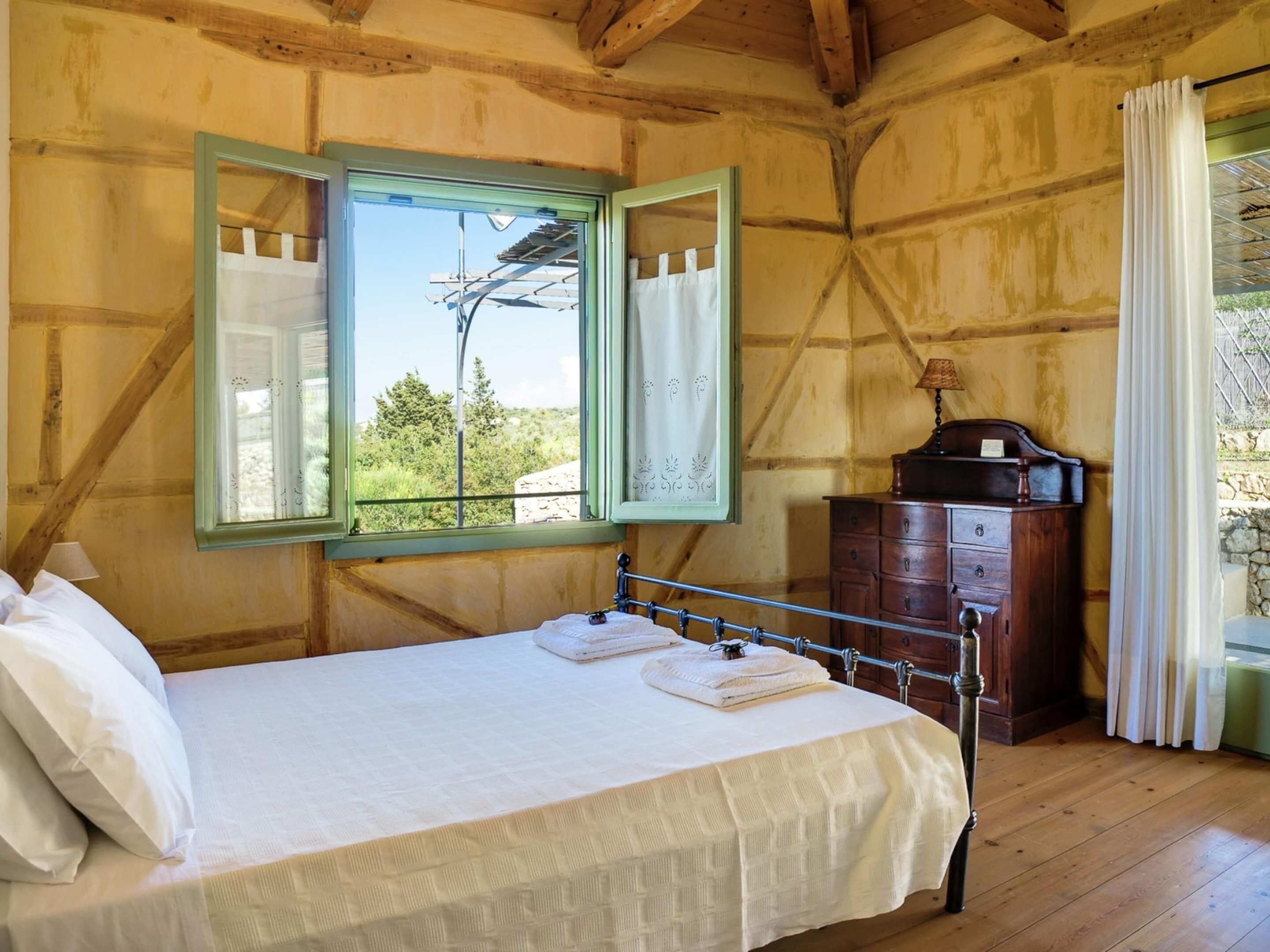 Een slaapkamer in een houten hutje, met een bed, een dressoir en een raam met gordijnen.