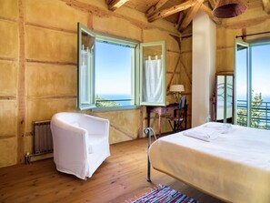 Relax in this serene bedroom with a large bed, a matching chair, and a charming view of the outdoors through open windows.