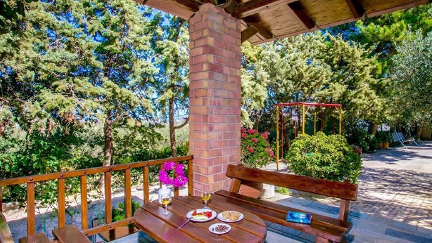 Um deck de madeira com uma mesa e bancos, cercado por árvores e um pilar de tijolos.