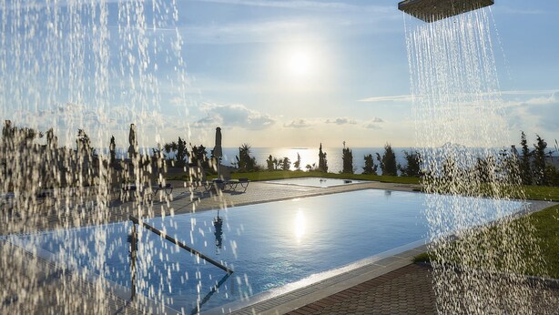 A pool with a water feature, surrounded by a landscaped area with trees and a view of the sea. - Villa in Kamilari Near Kid-friendly Beach (Faistos)
