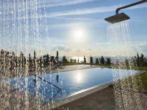 A pool with a water feature, surrounded by a landscaped area with trees and a view of the sea. - Villa in Kamilari Near Kid-friendly Beach (Faistos)