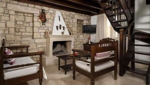 A cozy living room with a stone fireplace, wooden furniture, and a staircase. - Villa in Kamilari Near Kid-friendly Beach (Faistos)