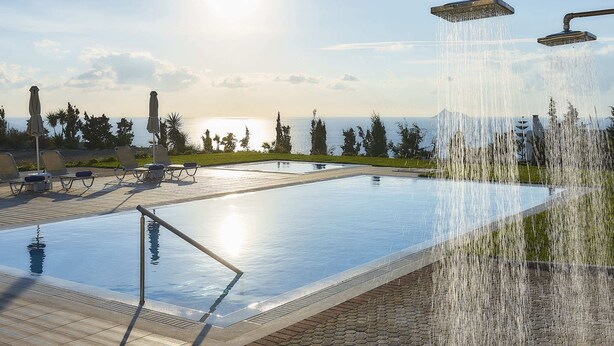 Una piscina infinita con caída de agua, rodeada de sillones de descanso y vistas al océano.