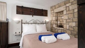 Un dormitorio con pared de piedra, una cama con ropa de cama blanca y cabecero de madera.
