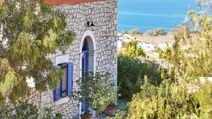 Un edificio de piedra con techo de cúpula roja, puerta azul y vista al mar.