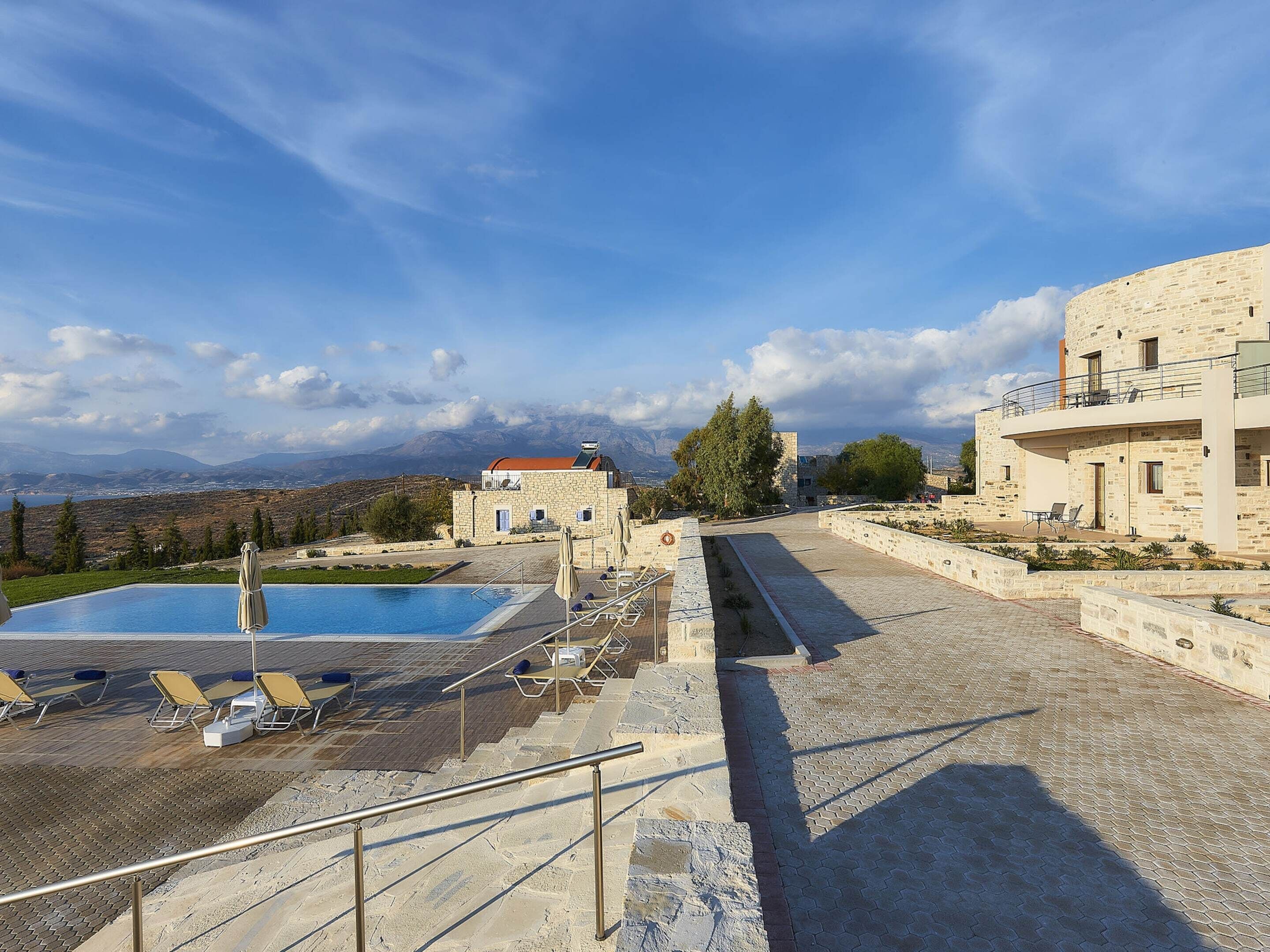 Un espace piscine doté de chaises longues et un bâtiment en pierre avec un balcon offrant une vue sur un paysage montagneux.