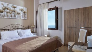 A hotel room with a bed, a desk with a chair, a wardrobe, a window with curtains, and a painting on the wall. - New Beautiful Complex With Villa's and App, Big Pool, Stunning Views, SW Crete (Faistos)