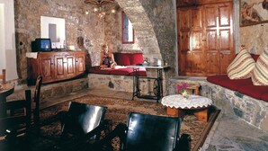 Une pièce rustique aux murs de pierre, avec un banc en bois, une table ornée d’un vase et un téléviseur posé sur un meuble.