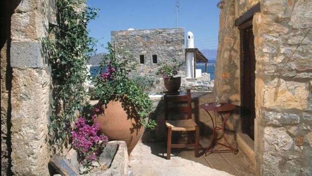 Un bâtiment en pierre doté d’un petit balcon, d’une chaise, d’une table et de plantes en pot.