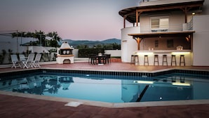 A modern outdoor pool area with a bar and seating, surrounded by a white building with a balcony.