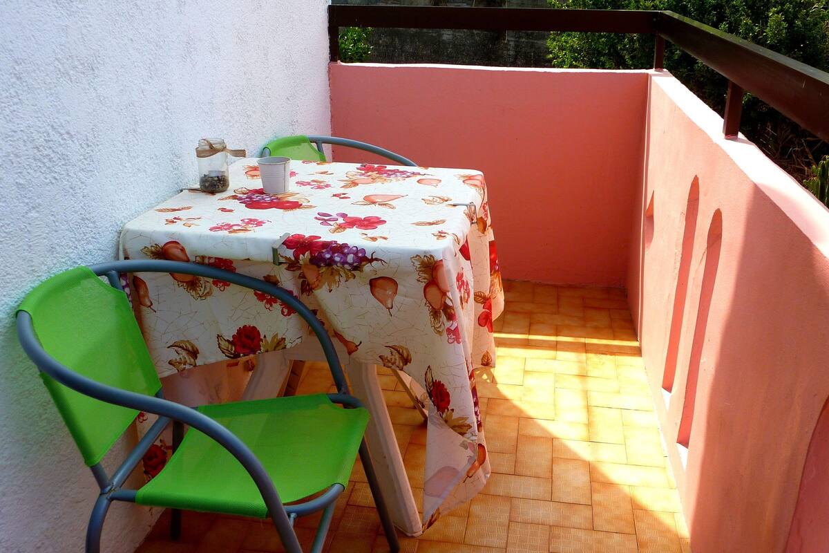 A small balcony with a table and two chairs, a tiled floor, and a pink wall.
