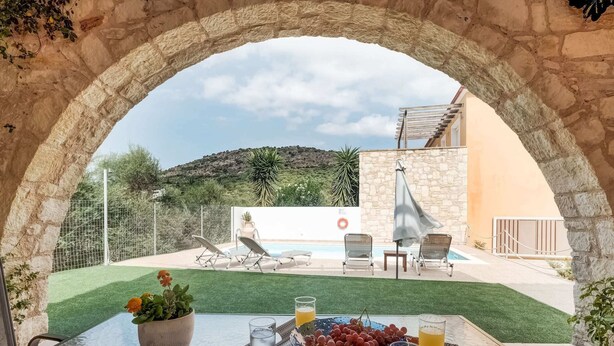 An outdoor seating area with a table, chairs, and a view of a swimming pool and hills. - Villa in Kalamitsi Near White Mountains (Apokoronas)