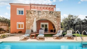A poolside area with lounge chairs and a stone archway leading to a covered patio. - Villa in Kalamitsi Near White Mountains (Apokoronas)