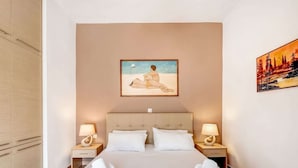 A hotel room with a large bed, two bedside tables with lamps, a painting of a woman on the wall, and a view of trees and a sunset. - Villa in Kalamitsi Near White Mountains (Apokoronas)