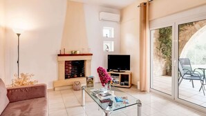 A modern living room with a fireplace, a flat-screen TV, and a glass coffee table. - Villa in Kalamitsi Near White Mountains (Apokoronas)