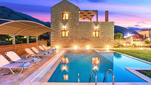 Un edificio de piedra con piscina, sillas de descanso y una zona cubierta.