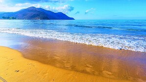Una playa con agua azul cristalina, una orilla arenosa y una montaña al fondo.